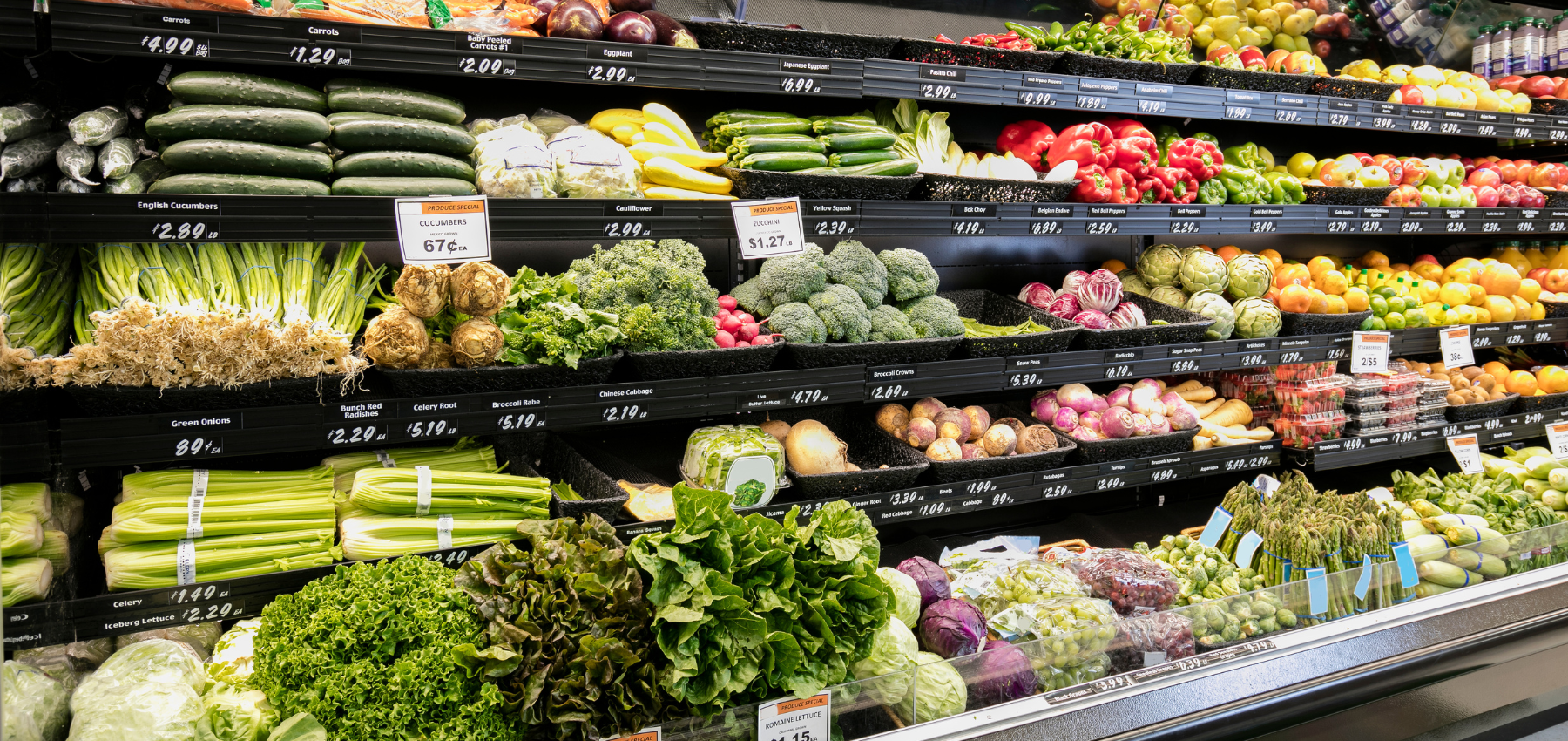 the produce aisle of a grocery store, filled with different produce such as broccoli, lettuce, green onions, celery, and red bell peppers